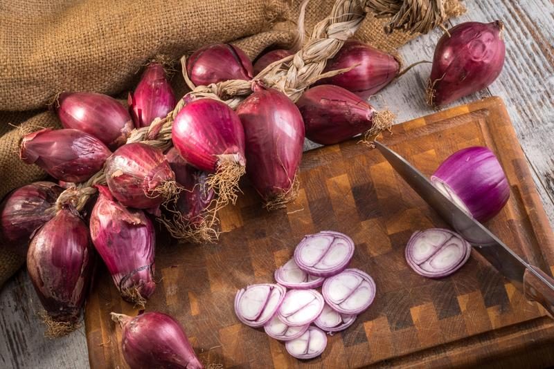 Oignons rouges de Tropea sur une planche de bois, coupés en tranches.