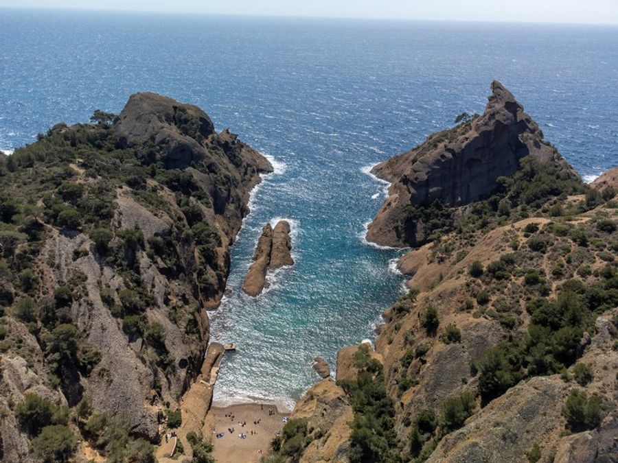 Vue aérienne des Calanques de Figuerolles avec leurs roches escarpées et une plage isolée.