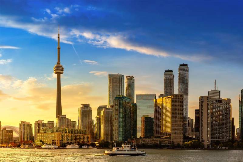 Skyline de Toronto au coucher du soleil, avec la tour CN en évidence et des bâtiments modernes reflétant la lumière dorée, vue depuis le lac Ontario.