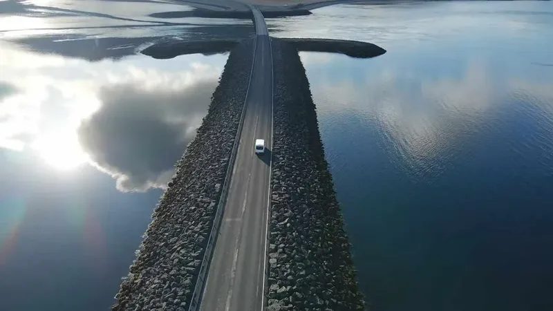 Route en Islande traversant l’océan avec une voiture blanche au centre