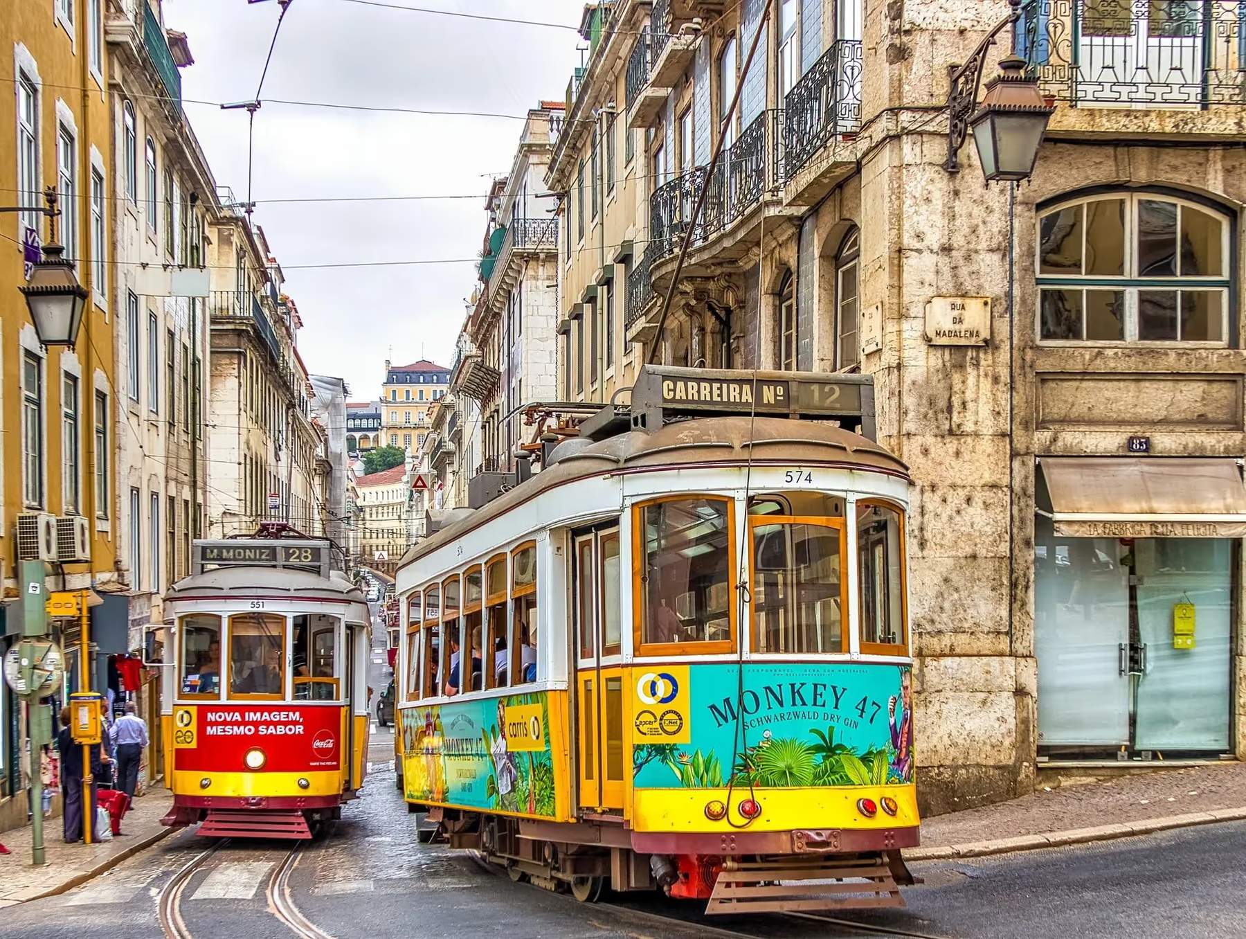 Tramways colorés roulant dans une rue étroite de Lisbonne, Portugal, avec des bâtiments historiques en arrière-plan.