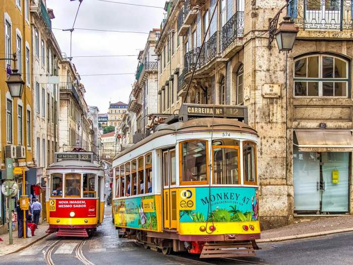 Tramways colorés roulant dans une rue étroite de Lisbonne, Portugal, avec des bâtiments historiques en arrière-plan.