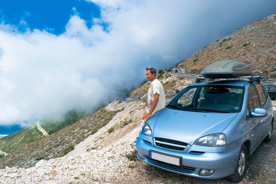 Voyageur appuyé sur sa voiture devant le panorama nuageux du Llogara Pass, Albanie