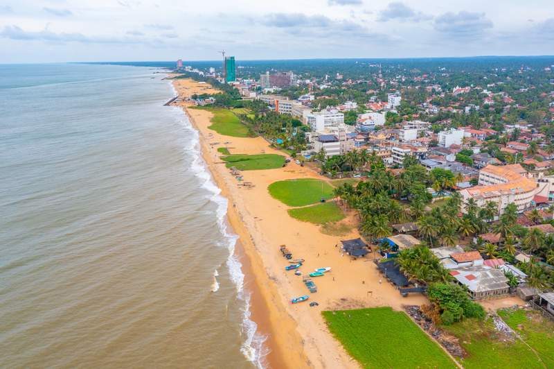 Plage de Negombo avec sable doré, bateaux de pêche et océan Indien en arrière-plan.