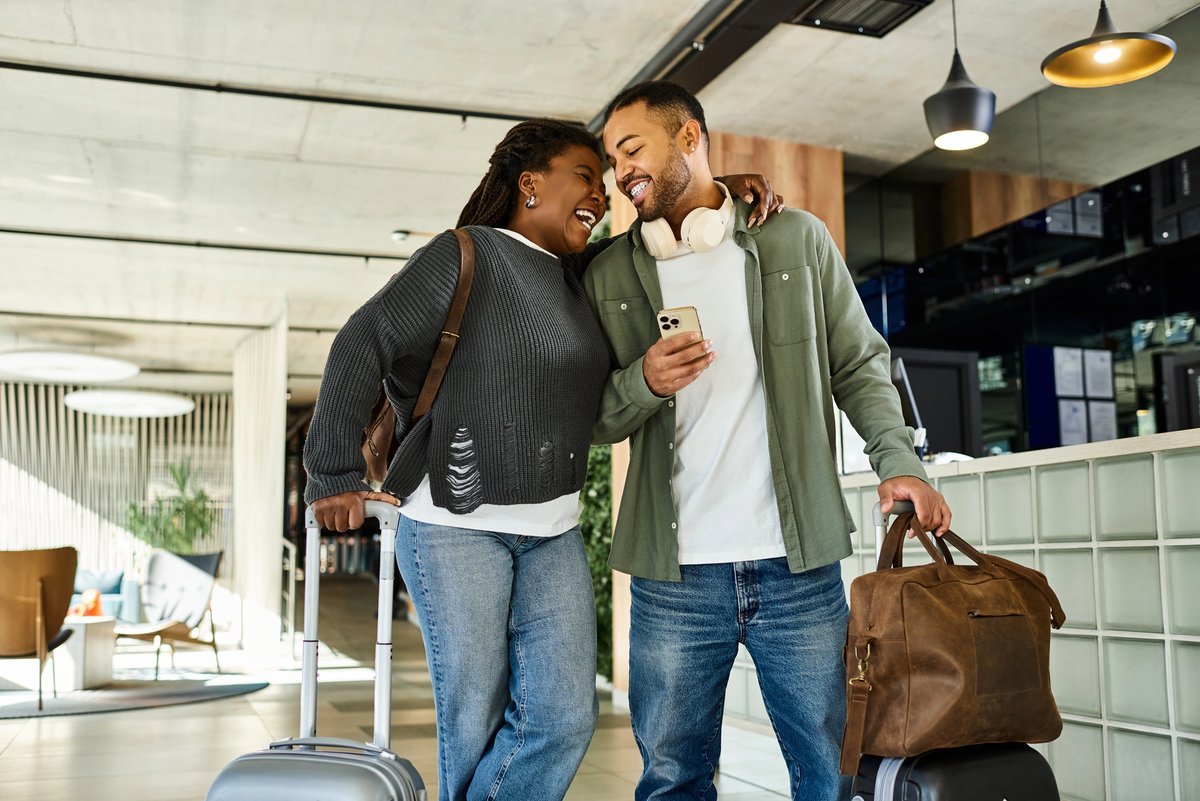 Un couple souriant arrive à l’hôtel avec ses valises, prêt pour un voyage de dernière minute.