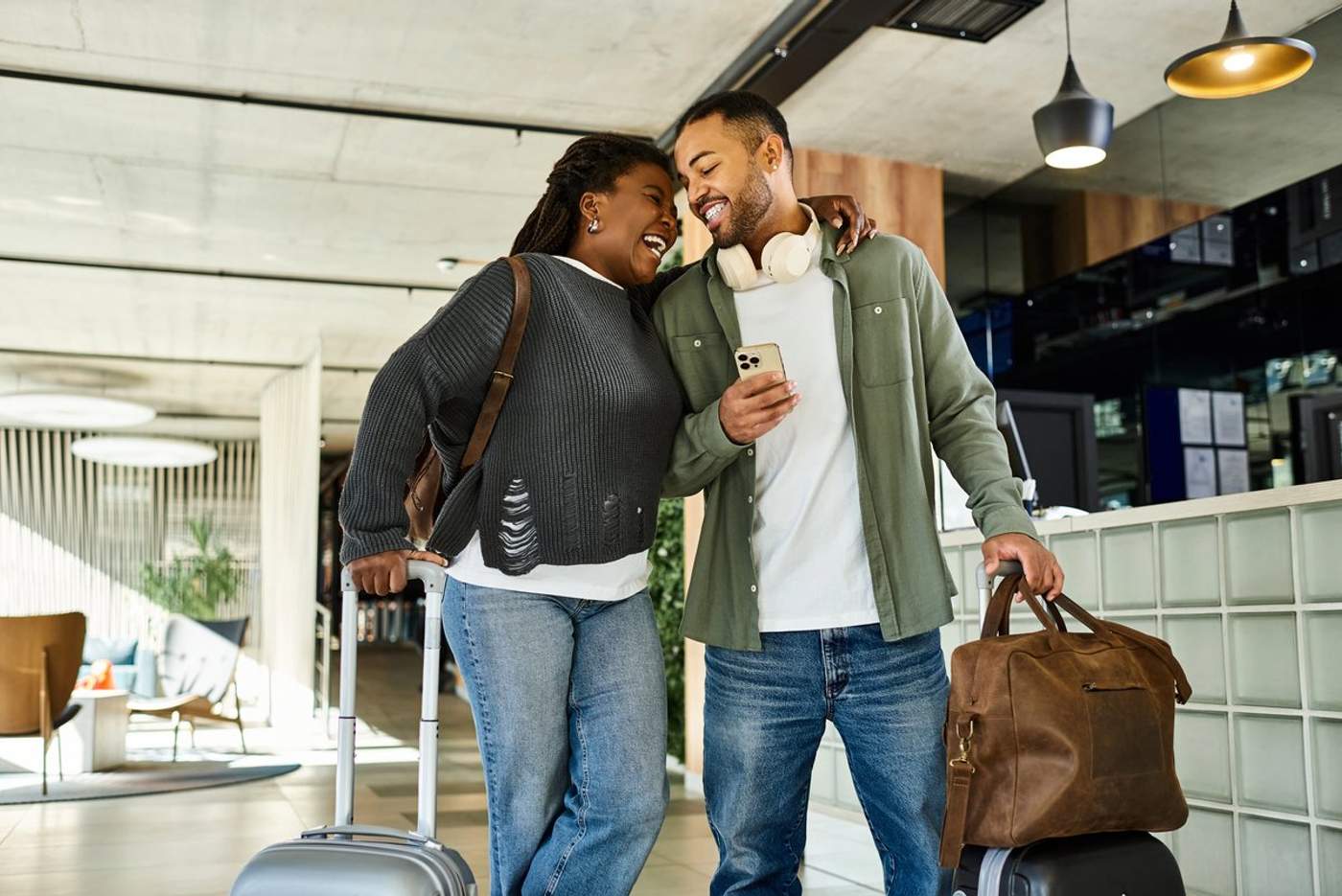 Un couple souriant arrive à l’hôtel avec ses valises, prêt pour un voyage de dernière minute.