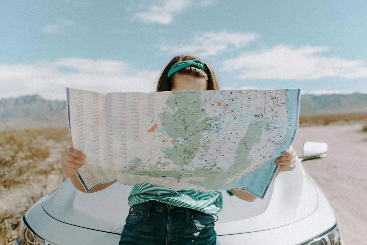 Une voyageuse se tenant debout devant une voiture tient une carte ouverte, à la recherche de son prochain arrêt sur un road trip.