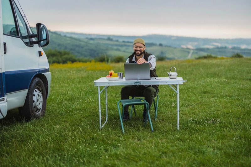 Nomade digital travaillant à distance depuis un van aménagé, ordinateur portable posé sur une table en pleine nature
