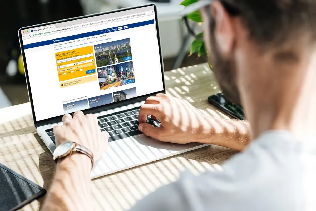 Homme consultant le site Booking.com sur un ordinateur portable pour réserver un hébergement en ligne.