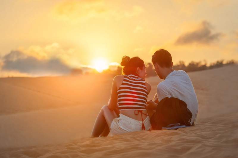Un couple assis sur une dune de sable au coucher du soleil, au Vietnam.