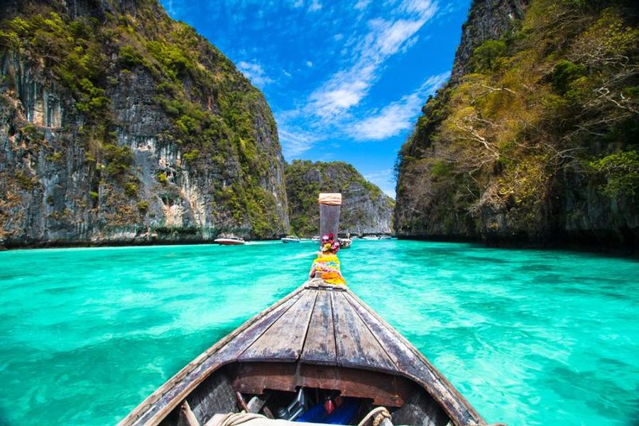 Un bateau traditionnel naviguant sur des eaux turquoise, entouré de falaises verdoyantes à Koh Phi Phi.
