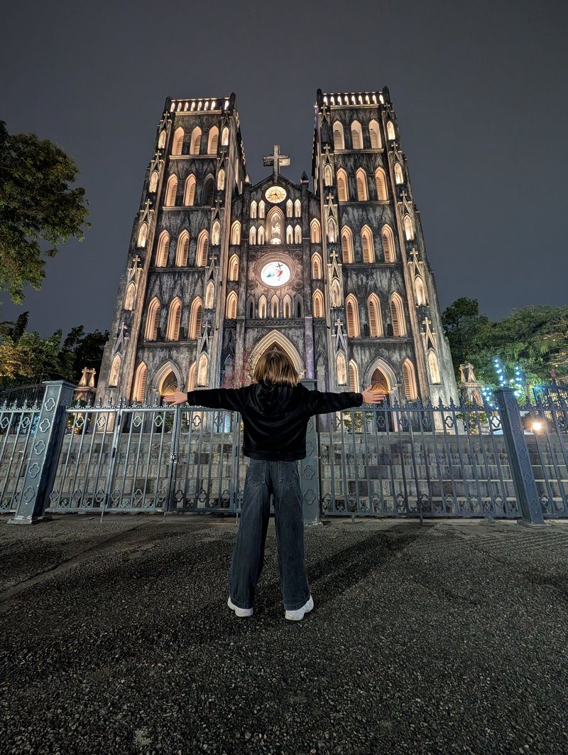 Vue nocturne de la cathédrale Saint-Joseph à Hanoï avec une fillette debout les bras ouverts.