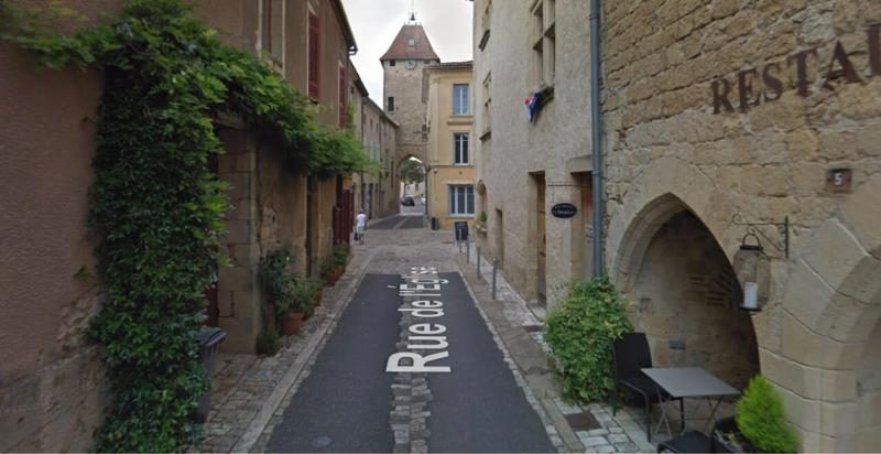 Ruelle pavée du village médiéval de Saint-Macaire avec des maisons en pierre et une tour au fond.