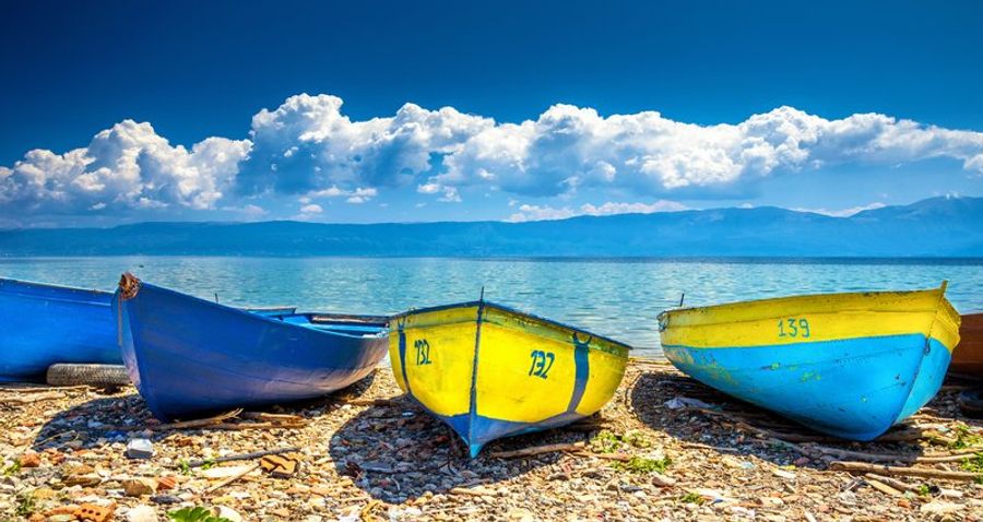Trois barques colorées alignées sur une plage de galets au bord du lac d
