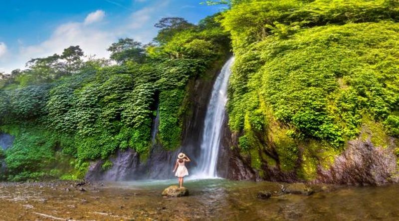 Voyageuse debout sur un rocher devant une grande cascade entourée d’une jungle dense à Bali.