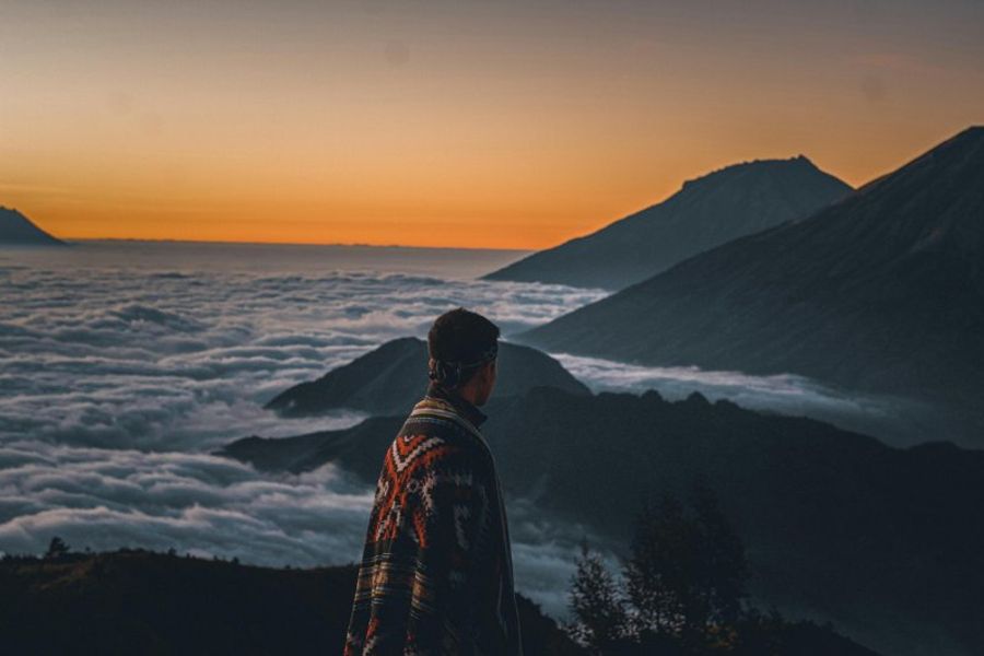 Personne observant le lever du soleil depuis le sommet du Mont Batur avec une mer de nuages.