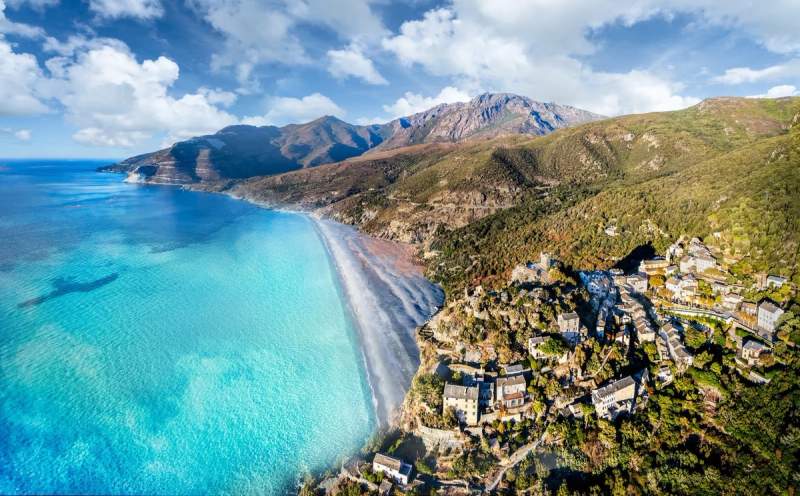 Vue aérienne de la plage de Nonza au Cap Corse, avec ses eaux turquoises et son village perché.