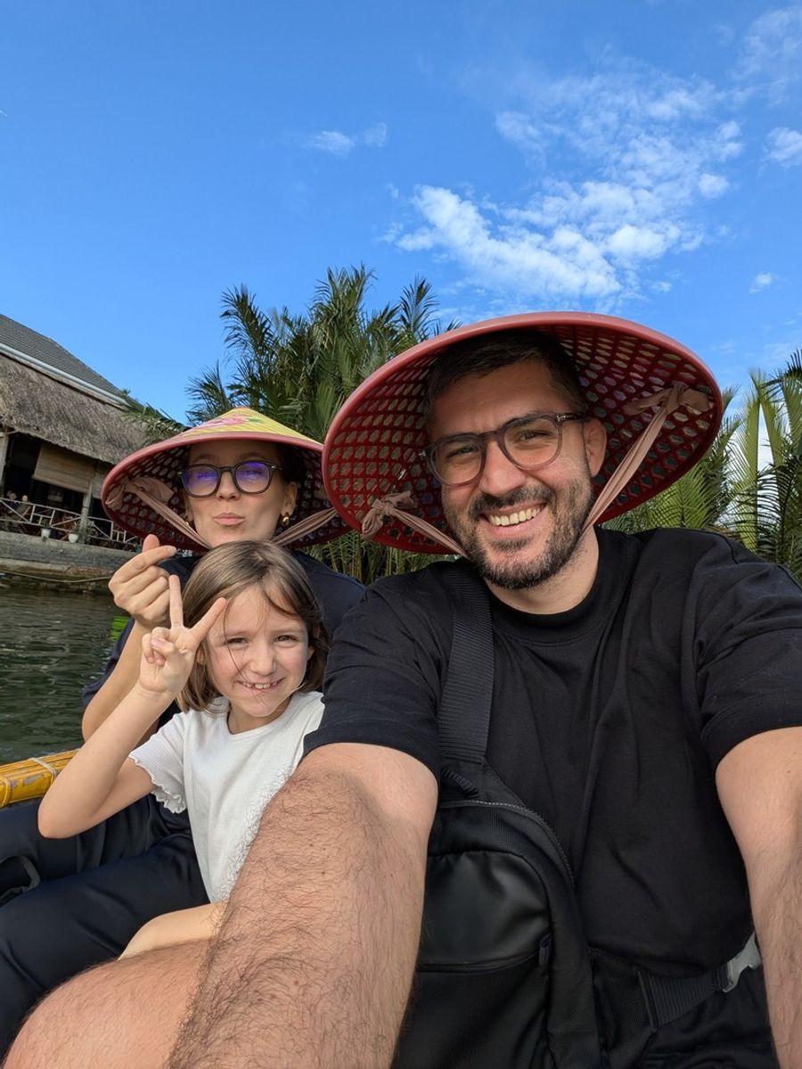 Famille souriante en bateau panier à Hoi An, Vietnam, portant les chapeaux traditionnels vietnamiens.