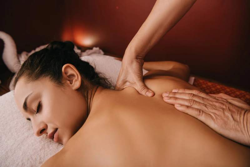 Femme recevant un massage relaxant dans un spa, allongée sur une table de massage avec une ambiance chaleureuse.