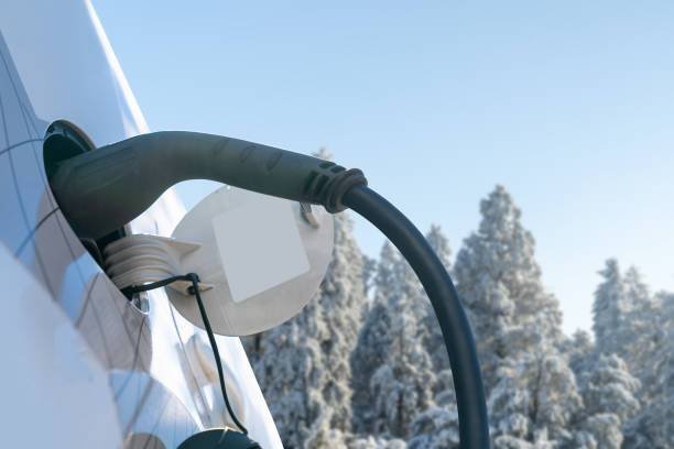 Câble de recharge connecté à une voiture électrique en hiver, avec une forêt enneigée en arrière-plan.