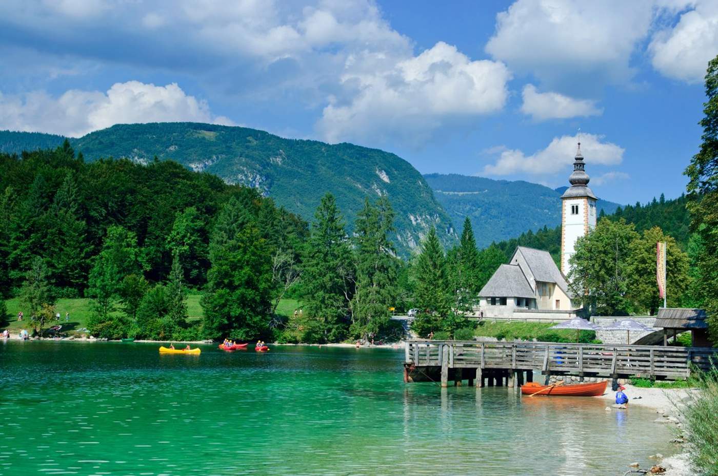 Lac de Bohinj en Slovénie avec ses eaux turquoise, des kayaks colorés et l'église Saint-Jean-Baptiste en arrière-plan