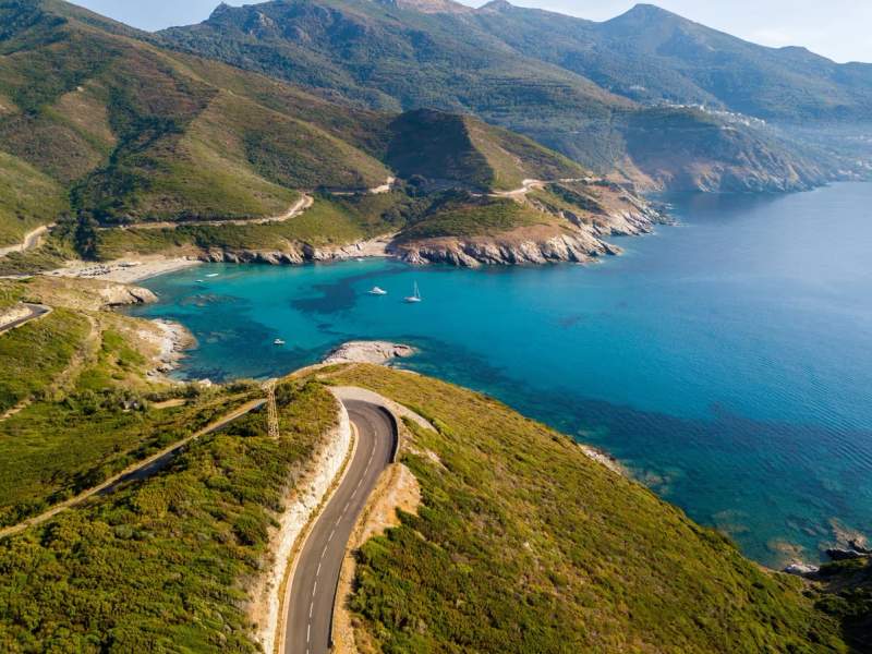 Route côtière sinueuse avec vue sur une mer turquoise au Cap Corse.