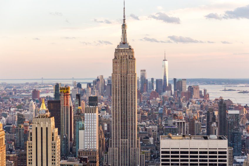 Vue panoramique de la ville de New York, mettant en avant l’Empire State Building au centre, avec des gratte-ciels et la skyline de Manhattan en arrière-plan au coucher du soleil.
