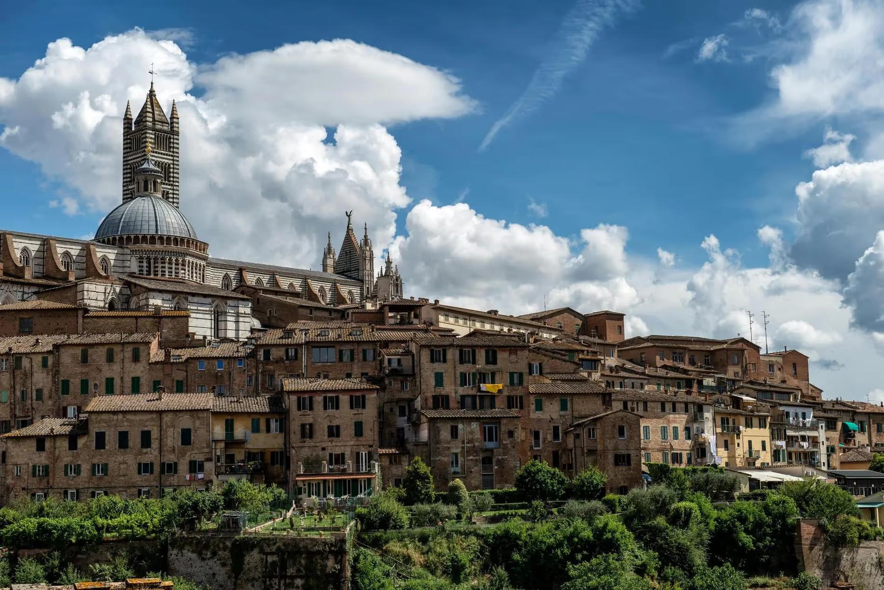Vue panoramique de la cathédrale de Sienne en Toscane, surplombant les maisons de la ville sous un ciel partiellement nuageux.