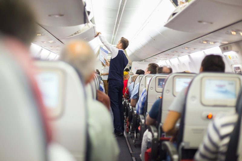 Steward dans un avion aidant les passagers à ranger leurs bagages dans les compartiments de cabine lors d