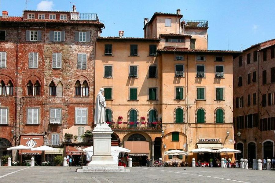 Piazza San Michele in Foro à Lucca avec des bâtiments historiques et une statue.