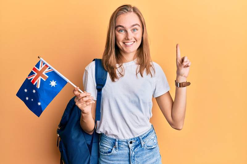 Étudiante souriante tenant un drapeau australien, prête à partir en séjour linguistique.