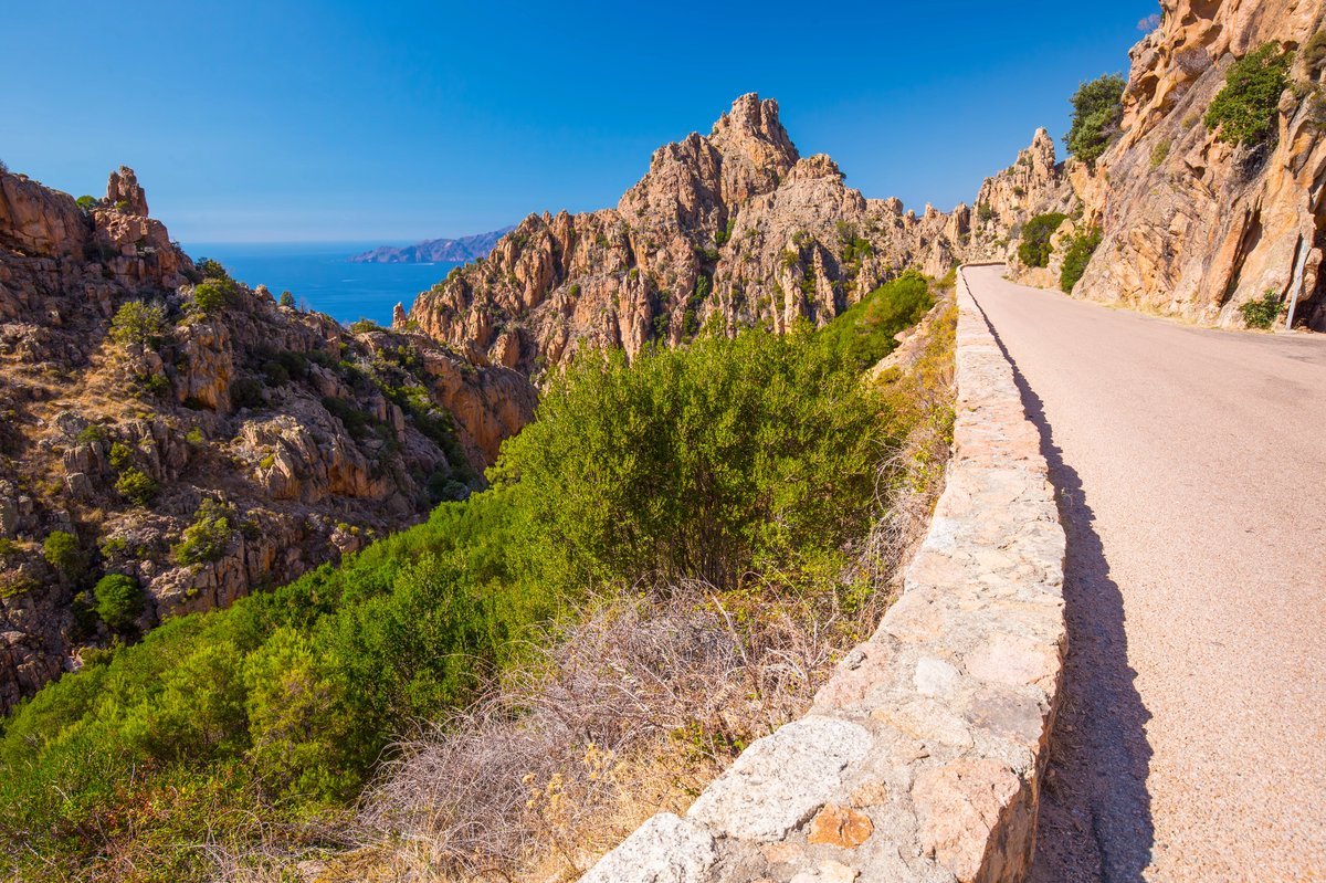 Route sinueuse dans les calanques de Piana, en Corse, surplombant la mer Méditerranée et les falaises rocheuses typiques de l’île de Beauté.