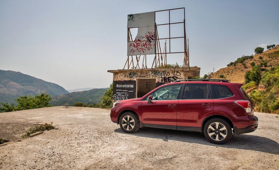 SUV rouge stationné sur une route de montagne en Albanie, paysage de collines boisées en arrière-plan