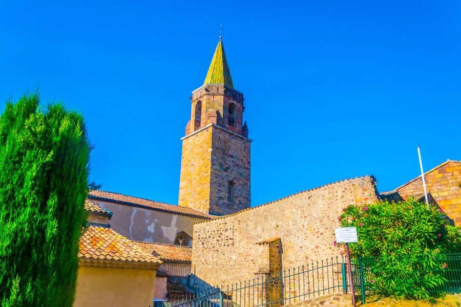 Tour élancée de la cathédrale de Fréjus avec un toit en tuiles vernissées, entourée d