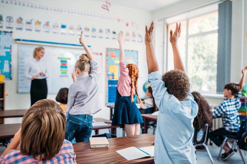 Enfants dans une salle de classe levant la main pour répondre à une question posée par l