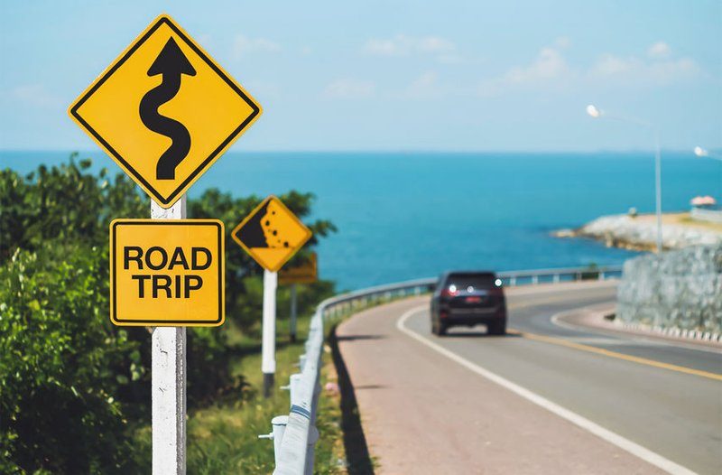 Panneau road trip sur une route côtière avec une voiture en arrière-plan