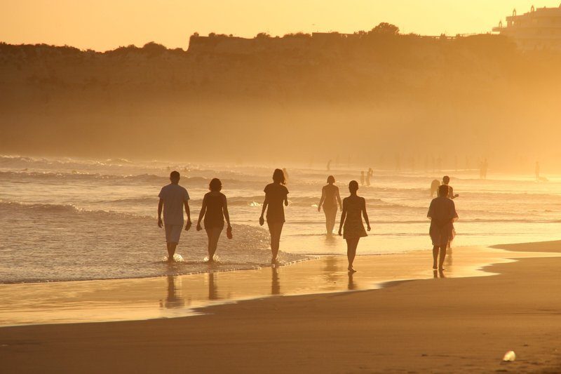 Promeneurs sur une plage au coucher de soleil au Portugal, avec des silhouettes se reflétant dans l