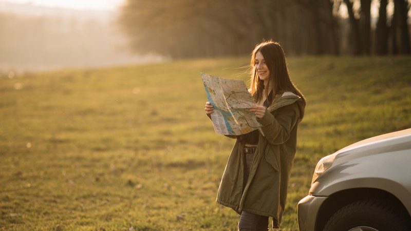 Femme consultant une carte au coucher du soleil près de sa voiture lors d’un road trip en pleine nature