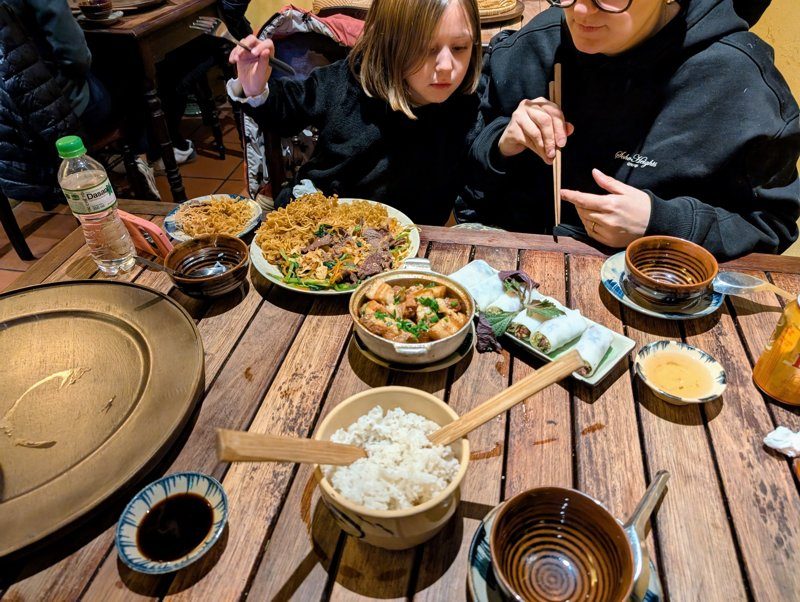 Repas vietnamien traditionnel avec nouilles, rouleaux de printemps, riz et plats mijotés sur une table en bois, partagé en famille à Hanoi.