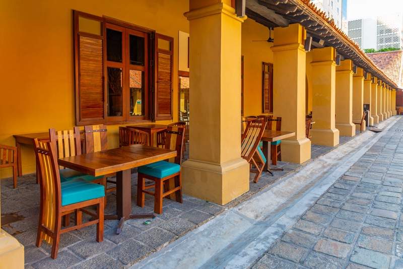 Terrasse de l’Old Dutch Hospital à Colombo avec tables en bois et piliers jaunes.