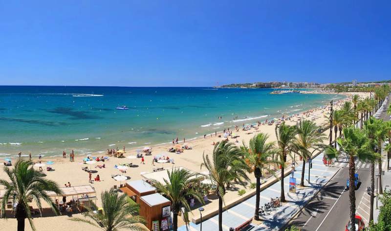 Vue panoramique de la plage de Salou avec des parasols, des palmiers et des baigneurs profitant du soleil.