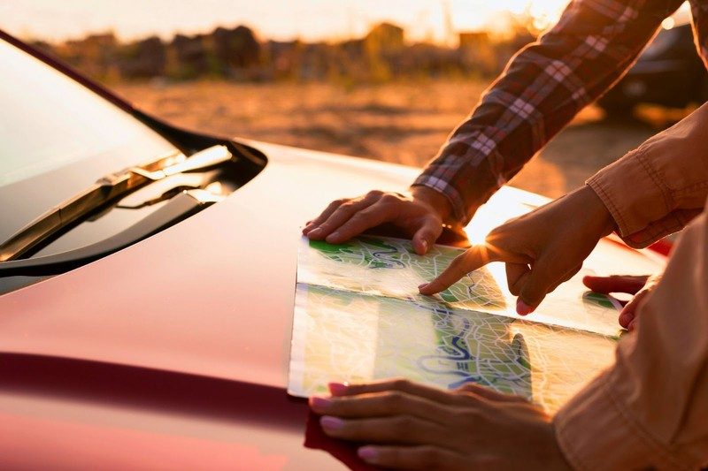 Deux personnes consultent une carte posée sur le capot d’une voiture au coucher du soleil lors d’un road trip.