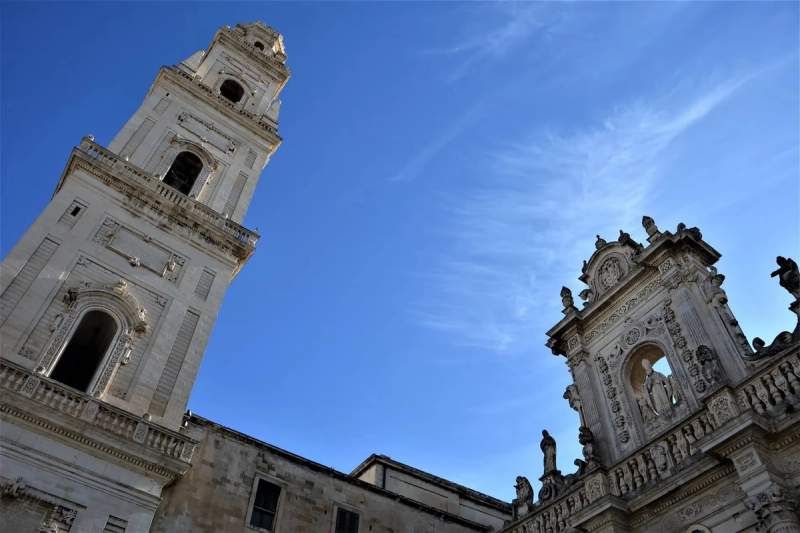 Tour et façade de la Piazza del Duomo sous un ciel bleu à Lecce, Italie.