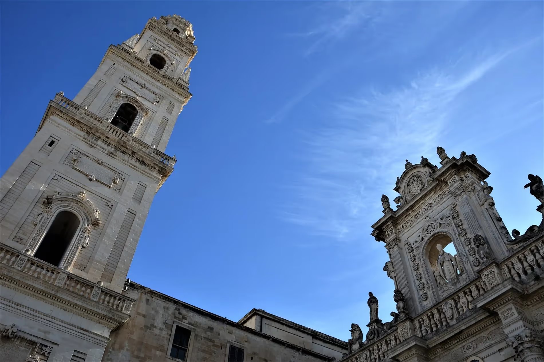 Tour et façade de la Piazza del Duomo sous un ciel bleu à Lecce, Italie.