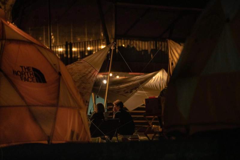 Deux personnes assises sous une tente éclairée dans un campement de nuit.