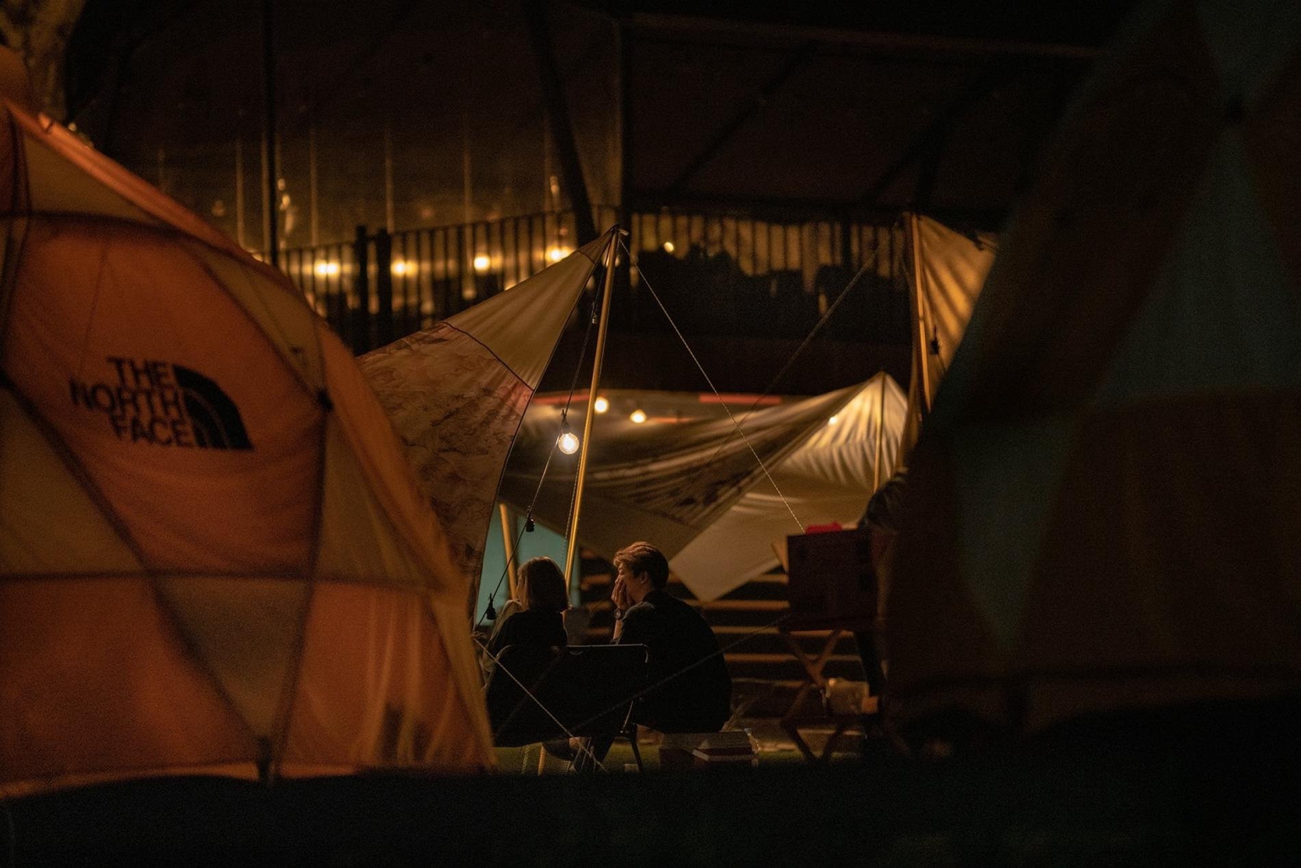 Deux personnes assises sous une tente éclairée dans un campement de nuit.