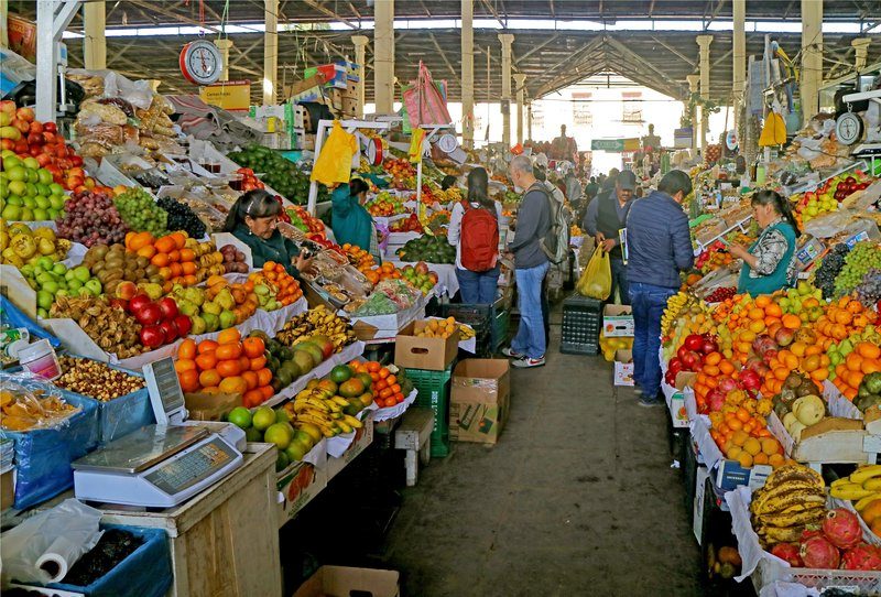 Étals de fruits colorés au marché San Pedro de Cusco, avec habitants et visiteurs faisant leurs courses