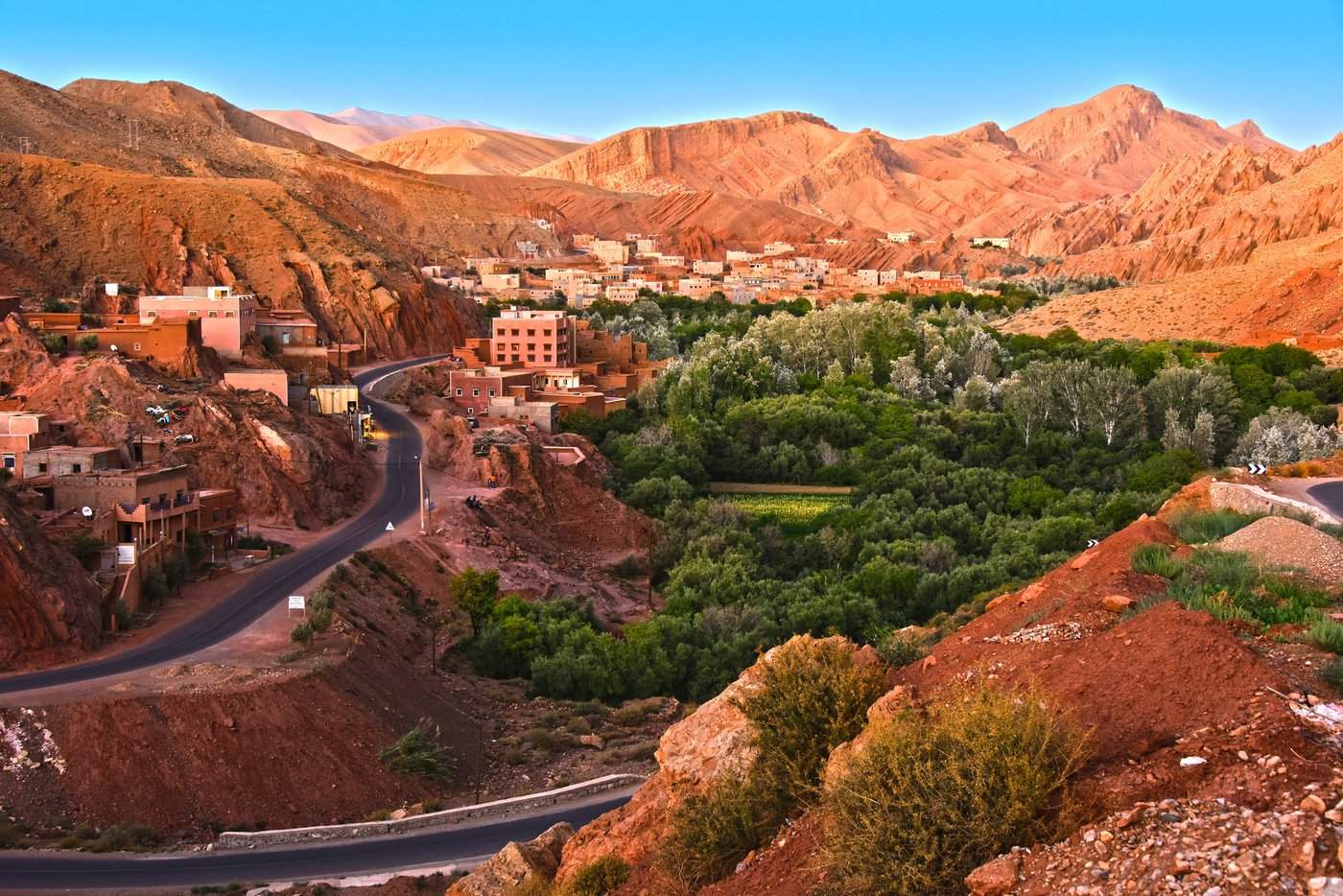 Vue panoramique d’un village marocain traditionnel niché entre des montagnes arides et une vallée verdoyante, au cœur d’une oasis.