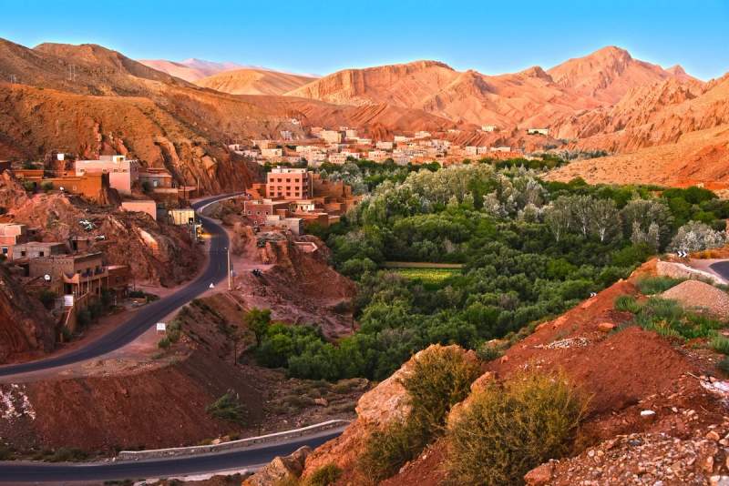 Vue panoramique d’un village marocain traditionnel niché entre des montagnes arides et une vallée verdoyante, au cœur d’une oasis.