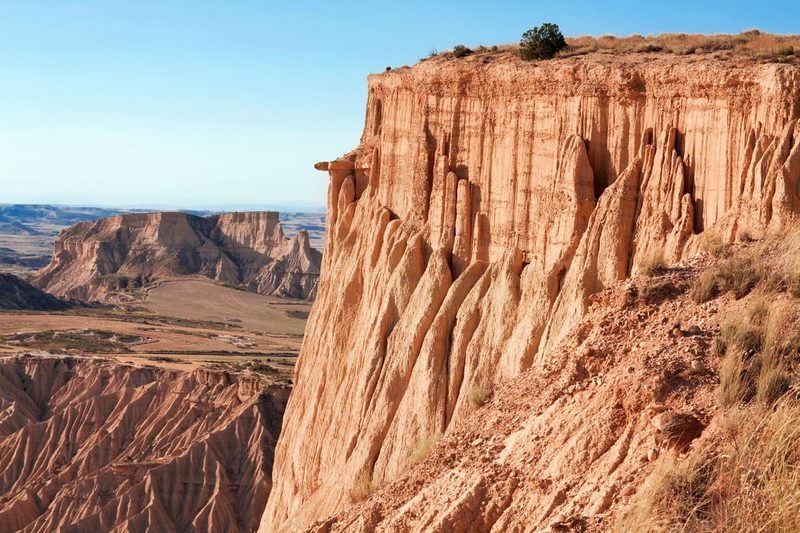 Falaises ocres sculptées par l'érosion dans le désert des Bardenas Reales, en Espagne, sous un ciel bleu clair.